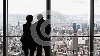 Silhouette from behind view of old senior couple looking beautiful view of urban city on top from window glass Editorial Stock Photo