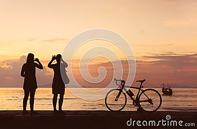 Silhouette bicycle and people take photo at beach sunset backgro Stock Photo