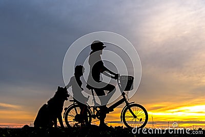 Silhouette biker lovely family at sunset over the ocean. Mom and daughter with dog bicycling at the beach. Stock Photo
