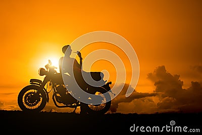 Silhouette of biker man sitting smokes with his motorbike beside the natural lake and beautiful, enjoying freedom and active lifes Stock Photo