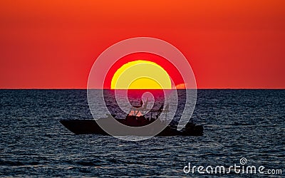 Silhouette of a boat swimming in the ocean with a vibrant sunset in Palm Jumeirah Stock Photo