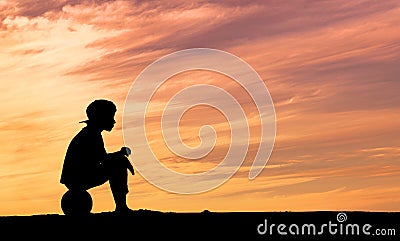 Silhouette of a boy sitting on football or soccer Stock Photo