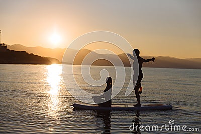 Silhouette of boy in yoga pose and girl sitting on sup surf at the ocean. Concept lifestyle, sport, love Stock Photo