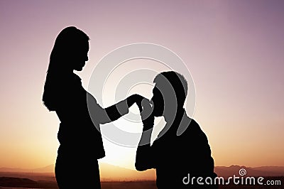 Silhouette of boyfriend kneeling and kissing his girlfriends hand at sunset Stock Photo