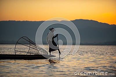 Silhouette of a burmese man wearing a hat Use the rowing legs to catch fish in the evening Editorial Stock Photo