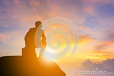 Silhouette of Business man kneeling position and looking forward on a mountain top Sunset Evening Sky Background, Success and acti Stock Photo