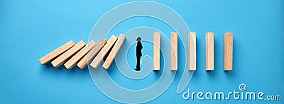 Silhouette of a businessman in apathy or inertia against collapsing wooden dominos on blue background. Business crisis and Stock Photo