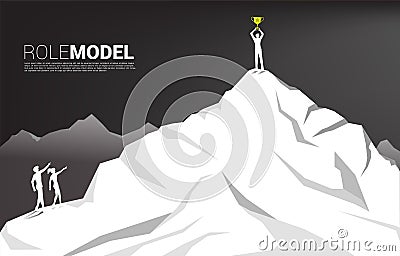 Silhouette of businessman and business woman point forward to businessman with trophy on top of mountain. Stock Photo