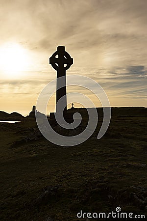 Silhouette of a Celtic cross with the evening sun. With a lighthouse, buildings and a cross in the background Stock Photo