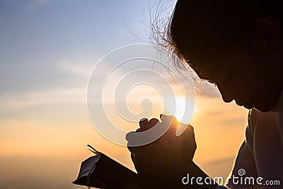 Silhouette of christian young woman praying with a cross and open the bible at sunrise, Christian Religion concept background Stock Photo