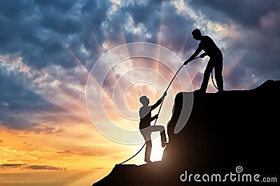 Silhouette climber helps to climb the top of another climber, throwing him a rope Stock Photo