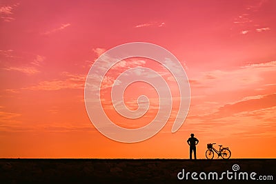 The silhouette of a cyclist against the background of the orange dawn sky. Stock Photo