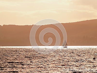 Silhouette distant hills and yacht sailing in under red sky at sunset Stock Photo