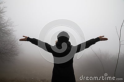 silhouette of a female with widely open hands looking towards fog mist Stock Photo