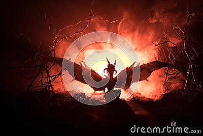 Silhouette of fire breathing dragon with big wings on a dark orange background. Horror image Stock Photo