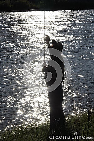 Silhouette of Fisherman at Dusk Checking his line Stock Photo