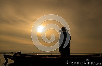 Silhouette of fisherman at sunrise, Standing aboard a rowing boat and casting a net to catch fish Stock Photo