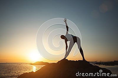 Silhouette fitness lady doing gymnastics by the ocean during a beautiful sunsetÑŽ Stock Photo