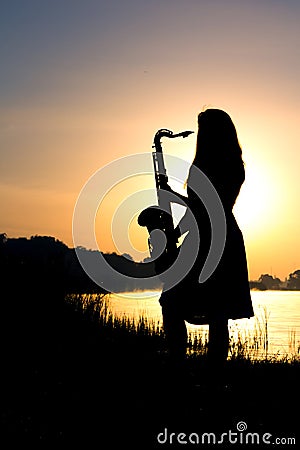 Silhouette of a girl in a dress with a brass musical instrument in his hands looking thoughtfully into the distance Stock Photo