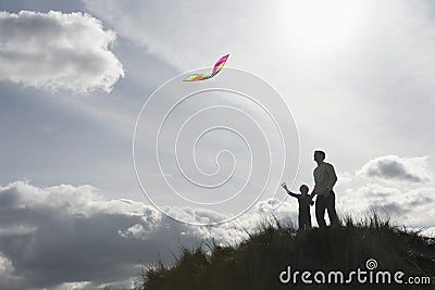 Silhouette of girl and father flying kite on dunes Stock Photo