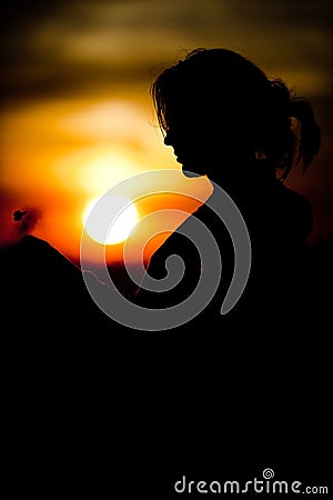 Silhouette of girl`s face holding cloverleaf during sunset - Black and orange colors Stock Photo