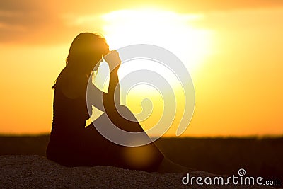 Silhouette of girl sitting on the sand and praying to God at sunset, the figure of young woman on the beach, concept religion Stock Photo