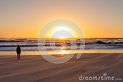 Silhouette girl watching a sunset on a sandy beach with rough ocean wind. Stock Photo