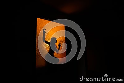 Silhouette of a girl's slim figure against a window with orange light Stock Photo