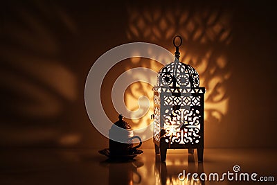 Silhouette of glowing Moroccan ornamental lantern with bronze tea cup. Decorative golden shadows. Greeting card Stock Photo