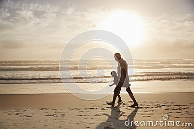 Silhouette Of Grandfather Walking Along Beach With Grandson Stock Photo