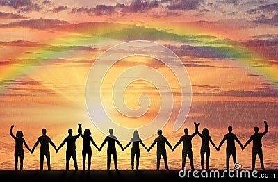 Silhouette of a group of happy people holding hands by the sea at sunset with a rainbow Stock Photo