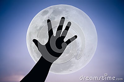 Silhouette of a hand with large full moon on fantastic sky background. Stock Photo