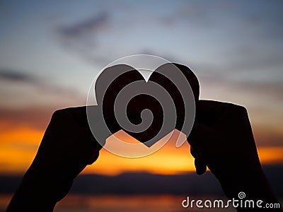 Silhouette hand is raising the red paper heart with blur sunlight during sunset, Stock Photo