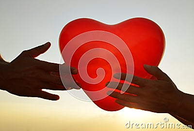 Silhouette of hands holding red balloon in the shape of heart. Stock Photo