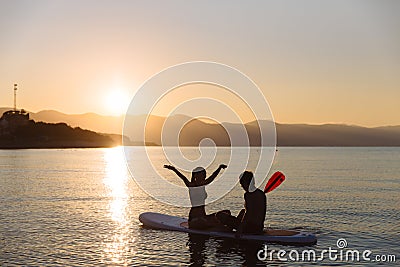 Silhouette of happiness boy and girl sitting on sup surf at the ocean. Concept lifestyle, sport, love Stock Photo