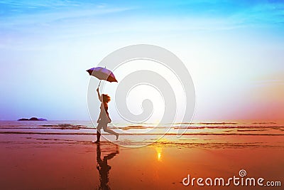 Silhouette of happy carefree girl with umbrella jumping on the beach Stock Photo