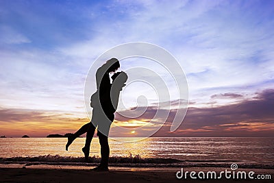 Silhouette of happy couple on paradise beach at sunset, man taking the girl in his arms Stock Photo