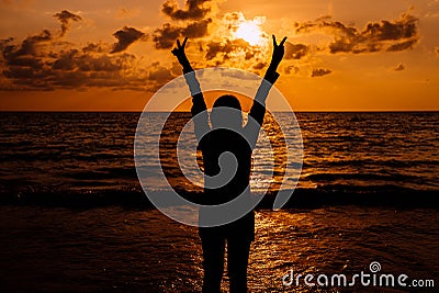 Silhouette of Happy woman showing two fingers while sunset at sea,Overcoming obstacle concept Stock Photo