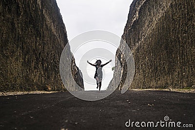 Silhouette on the horizon of young happy and active woman running and jumping excited on road between mountain cliffs feeling free Stock Photo