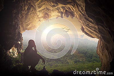Silhouette humble man sitting on a rock in cave looking at birds Stock Photo