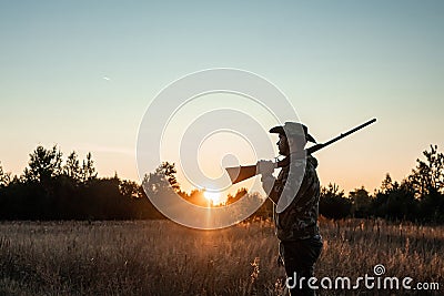 Silhouette of a hunter in a cowboy hat with a gun in his hands on a background of a beautiful sunset. The hunting period, the fall Stock Photo