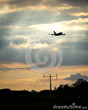 Silhouette of jumbo jet flying at sunset behind high tech radio mast for communications between pilot and airport Stock Photo