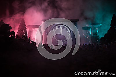 Silhouette of a large crowd of people in forest at night standing against a big arrow clock with toned light beams on foggy backgr Stock Photo