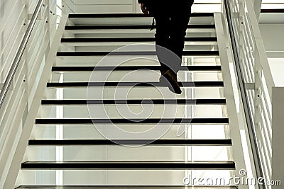 Silhouette of legs and feet of a man climbing up the black steps of a modern open staircase Stock Photo