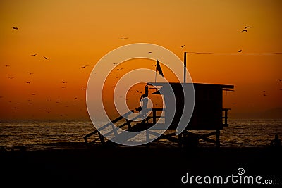 Silhouette of a lifeguard in his tower watching the coast, orange sunset at Santa Monica., California, USA Stock Photo