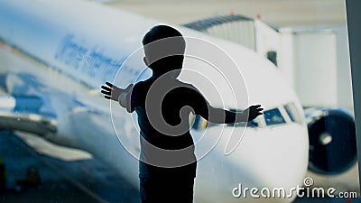 Silhouette of little boy looking on big airplane through big window in airport terminal Stock Photo