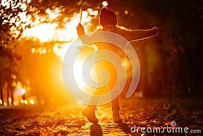 Silhouette of little girl with feather in hand, dancing in setting sun Stock Photo