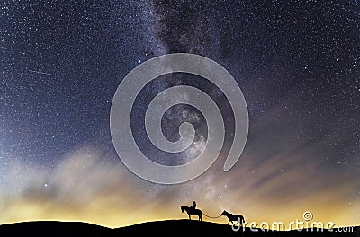 Silhouette of a lone rider with a horses walking on a hill in the starry night. Behind him is the beautiful bright Milky Way galax Stock Photo