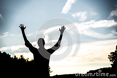 Silhouette of a male with his hands up towards the sky with a blurred background Stock Photo