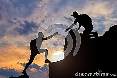 Silhouette of a male mountaineer working in a team with a partner, giving him a helping hand Stock Photo